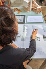  Young woman works as an architect in an office. She is brunette and Latina has a black shirt and different jobs on her table.