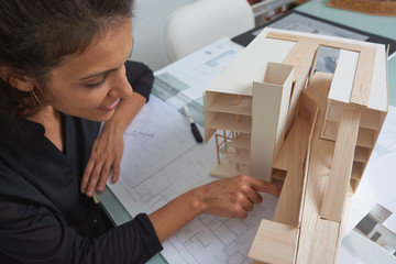  Young woman works as an architect in an office. She is brunette and Latina has a black shirt and different jobs on her table.