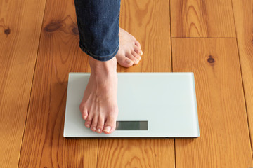木目の床と体重計に乗る若い女性の足元