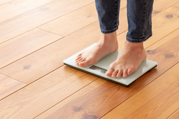 Fototapeta na wymiar 木目の床と体重計に乗る若い女性の足元