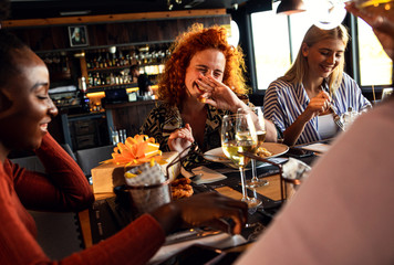 Group of young female friends having fun in restaurant, talking and laughing while dining at table.