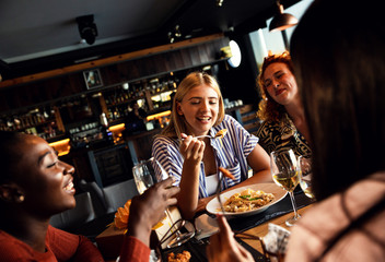 Group of young female friends having fun in restaurant, talking and laughing while dining at table.
