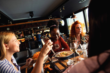 Group of young female friends having fun in restaurant, talking and laughing while dining at table.