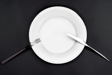 Table setting. Empty plate, knife and fork on a black background. Fork and knife are on the plate, pause in food. Top view and flat lay with copy space