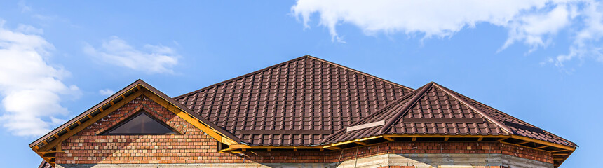The roof of the house from a metal profile against the sky with clouds