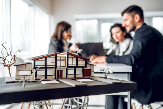 Close up image of house model with group business people on blurred background in building design studio. Architecture project concept