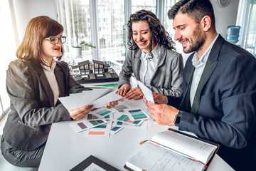 Side view of smiling business handsome man and attractive woman choosing color for their new house with help of female design advisor. Customers in real estate agency office. Work with clients concept
