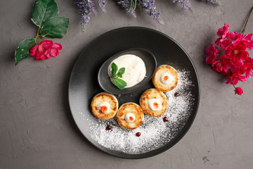 pancakes with sour cream in a black plate decorated with icing sugar