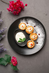 pancakes with sour cream in a black plate decorated with icing sugar