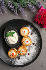 pancakes with sour cream in a black plate decorated with icing sugar