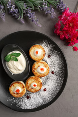 pancakes with sour cream in a black plate decorated with icing sugar