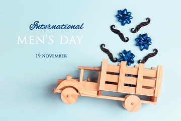 International men's day card with wooden toy truck with mustache and bows in the back on blue background. F