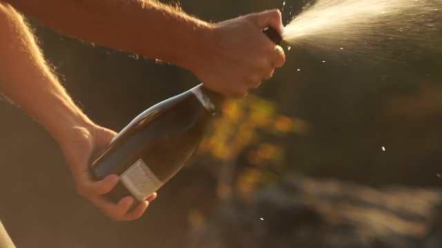 Man opens champagne bottle. Champagne explosion. Champagne popping. Sparkling Wine on sunset sunrise outdoors. Man shakes a bottle splashing champagne