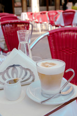 Glass cup of coffee on the table. Summer outdoor cafe with red furniture. Reflection of a city in a teaspoon.