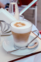 Glass cup of coffee on the table. Summer outdoor cafe. Reflection of a city in a teaspoon.