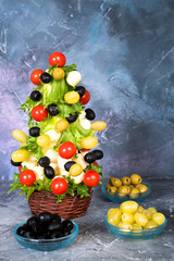 Christmas edible tree made from lettuce, tomatoes, olives and grapes with mozzarella cheese. Food art concept. New Year food.