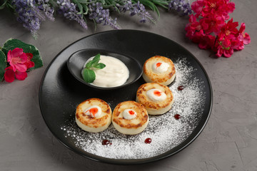 pancakes with sour cream in a black plate decorated with icing sugar