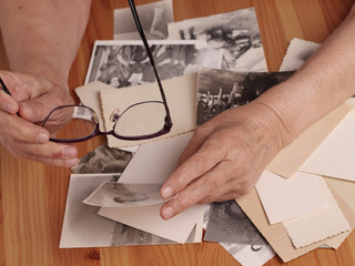 An elderly woman looks at old photographs, recalls her past youth. Hands on the table. Loneliness,, memories.