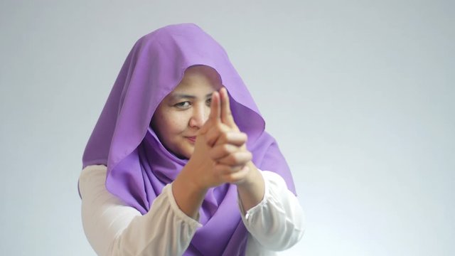 Beautiful Asian muslim lady looking at camera, pointing smiling and doing pistol gun shoot gesture with fingers