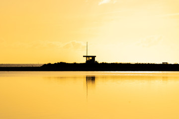 Golden hour on the ocean: The beach with a baywatch tower covered in golden light, the ocean reflecting the sunlight