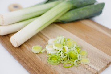 Fresh Leeks and leek round cuttings in a wooden board in a white background © Juana