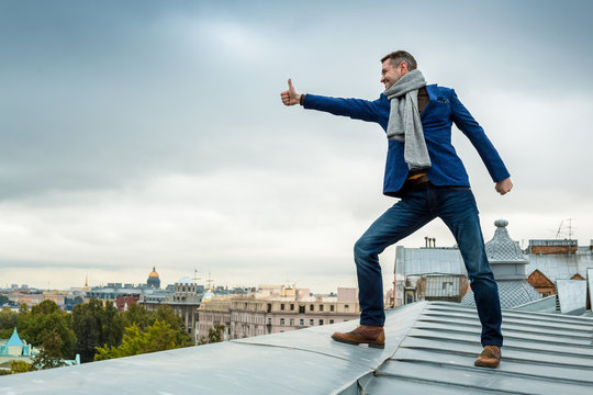 A young man on the roof of the building shows a gesture with his hand - it's good, it's cool, thumb up. An inspired tourist enjoys a rooftop sightseeing tour of a European city. St. Petersburg, Russia