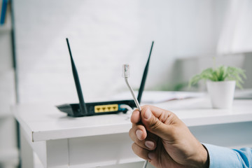 cropped view of businessman holding wire with connector near router