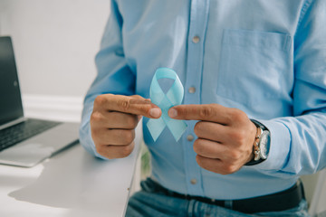 partial view of man in blue shirt holding blue awareness ribbon