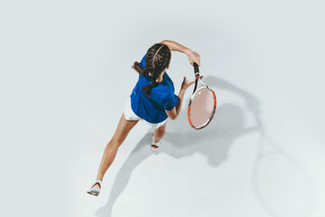 Young woman in blue shirt playing tennis. She hits the ball with a racket. Indoor studio shot...