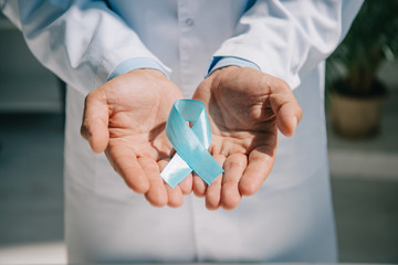 cropped view of doctor in white coat holding blue awareness ribbon