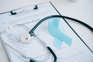 medical report, stethoscope and blue awareness ribbon on white table