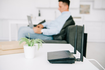 selective focus of black router on white desk near flowerpot and businessman using laptop