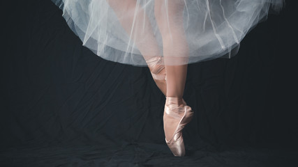 Close-up of dancing legs of ballerina wearing white pointe on a black background.