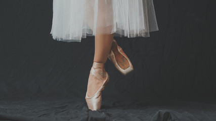 Close-up of dancing legs of ballerina wearing white pointe on a black background.