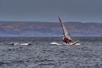A male athlete is interested in windsurfing. He moves on a Sailboard on a large lake on an autumn...