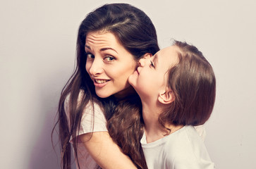 Happy casual kid girl whispering the secret to her smiling mother in ear with fun face on purple background. Closeup