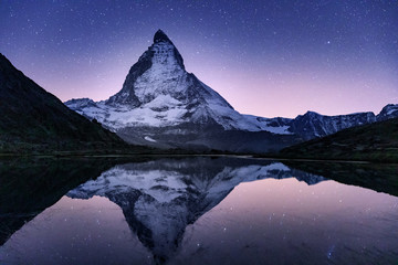Starry night landscape, famous mounatin peak Matterhorn in Switzerland reflecting in mountain lake.