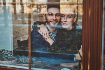 Attractive couple of romantic people are sitting in cafe and looking through the window.