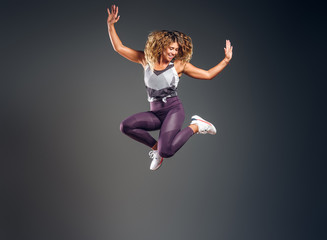 Happy attractive woman in activewear is jumping at studio over grey background.