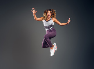 Cheerful happy woman is showing her performance at photo studio on the grey background.