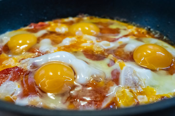 Freshly cooked appetizing fried eggs with red sweet tomatoes in a hot pan. Delicious homemade food.