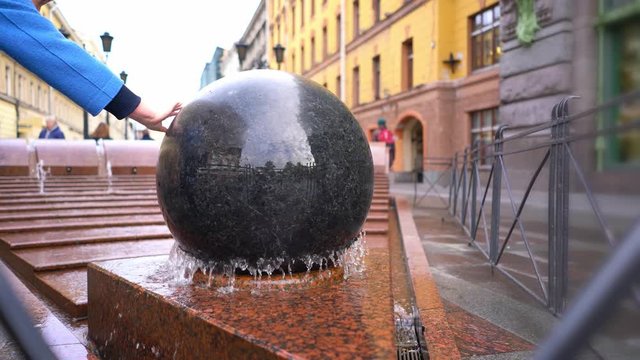 a round large marble ball in water spins, a landmark is a statue of a ball in a fountain.