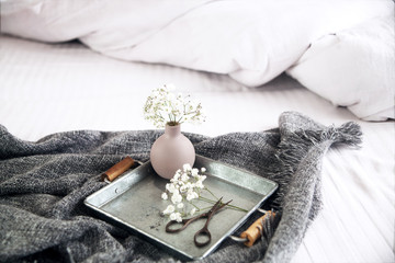 a beautiful small vase, a metal tray on a bed with white bedding