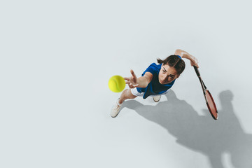 Young woman in blue shirt playing tennis. She hits the ball with a racket. Indoor studio shot isolated on white. Youth, flexibility, power and energy. Negative space. Top view. © master1305
