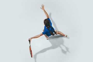 Naklejka premium Young woman in blue shirt playing tennis. She hits the ball with a racket. Indoor studio shot isolated on white. Youth, flexibility, power and energy. Negative space. Top view.