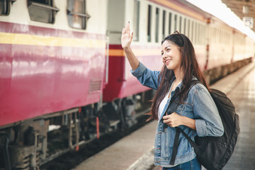 Portrait of an Asian woman smiling and waving goodbye at the train station. Tourism concept