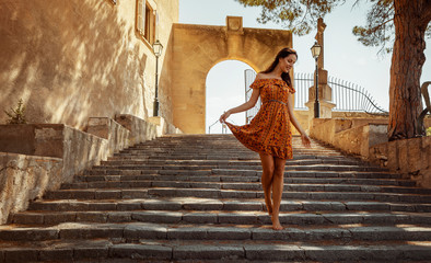 young brunette woman wearing a floral pattern summer dress, walking down a staircase, at a castle...