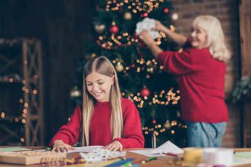 Fototapeta premium Portrait of nice attractive creative talented cheerful granny pre-teen grandchild hanging paper flake creating festive decor on table decorated industrial brick wood loft style lights interior house