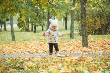 A little girl in ayellow coat is playing with falling leaves