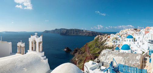 panoramic view of the Santorini caldera and Oia, with a church bell tower and iconic blue church...